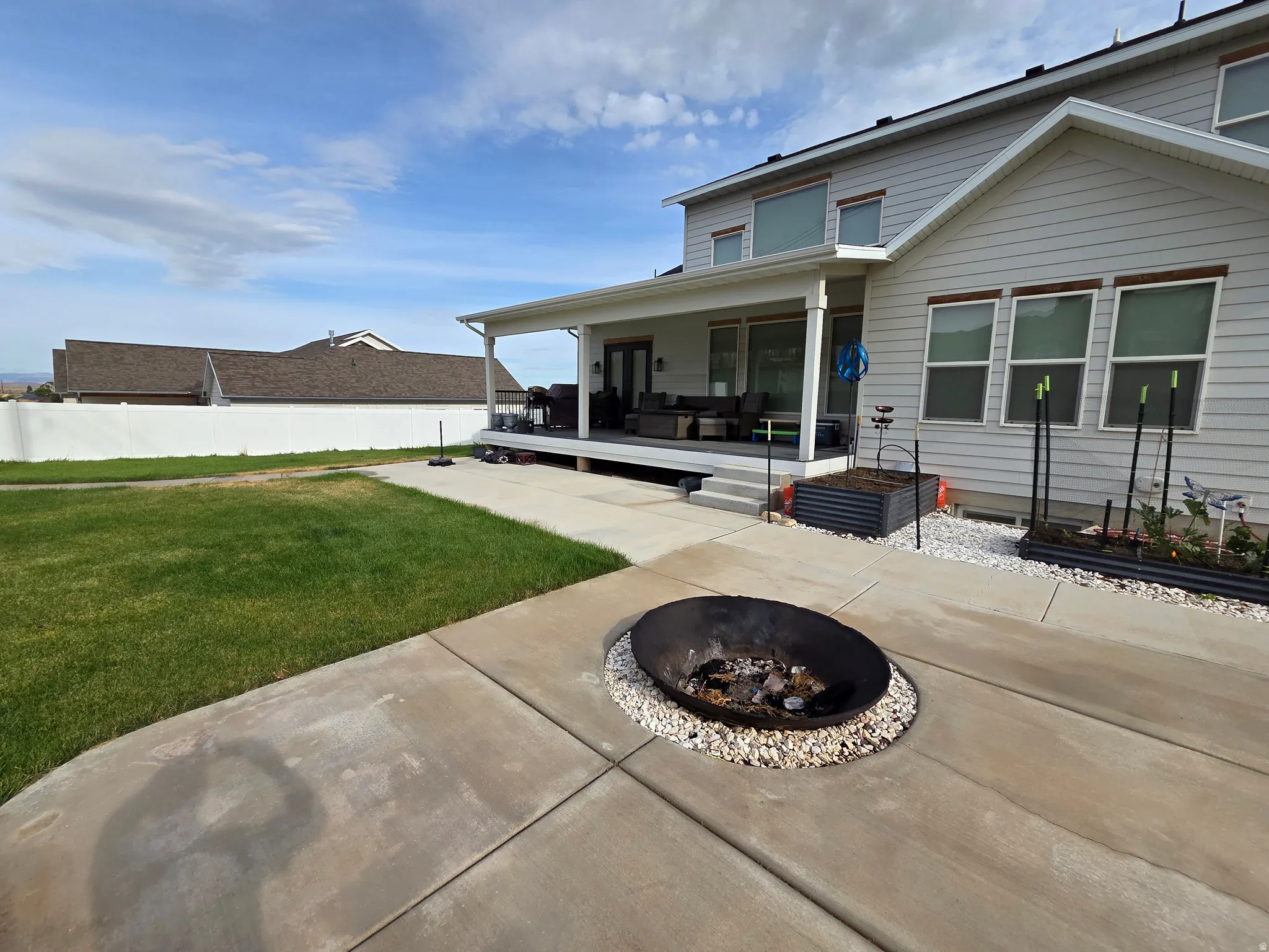 Expansive concrete patio with integrated fire pit surrounded by decorative stone edging, adjoining manicured lawn and covered rear porch with column supports