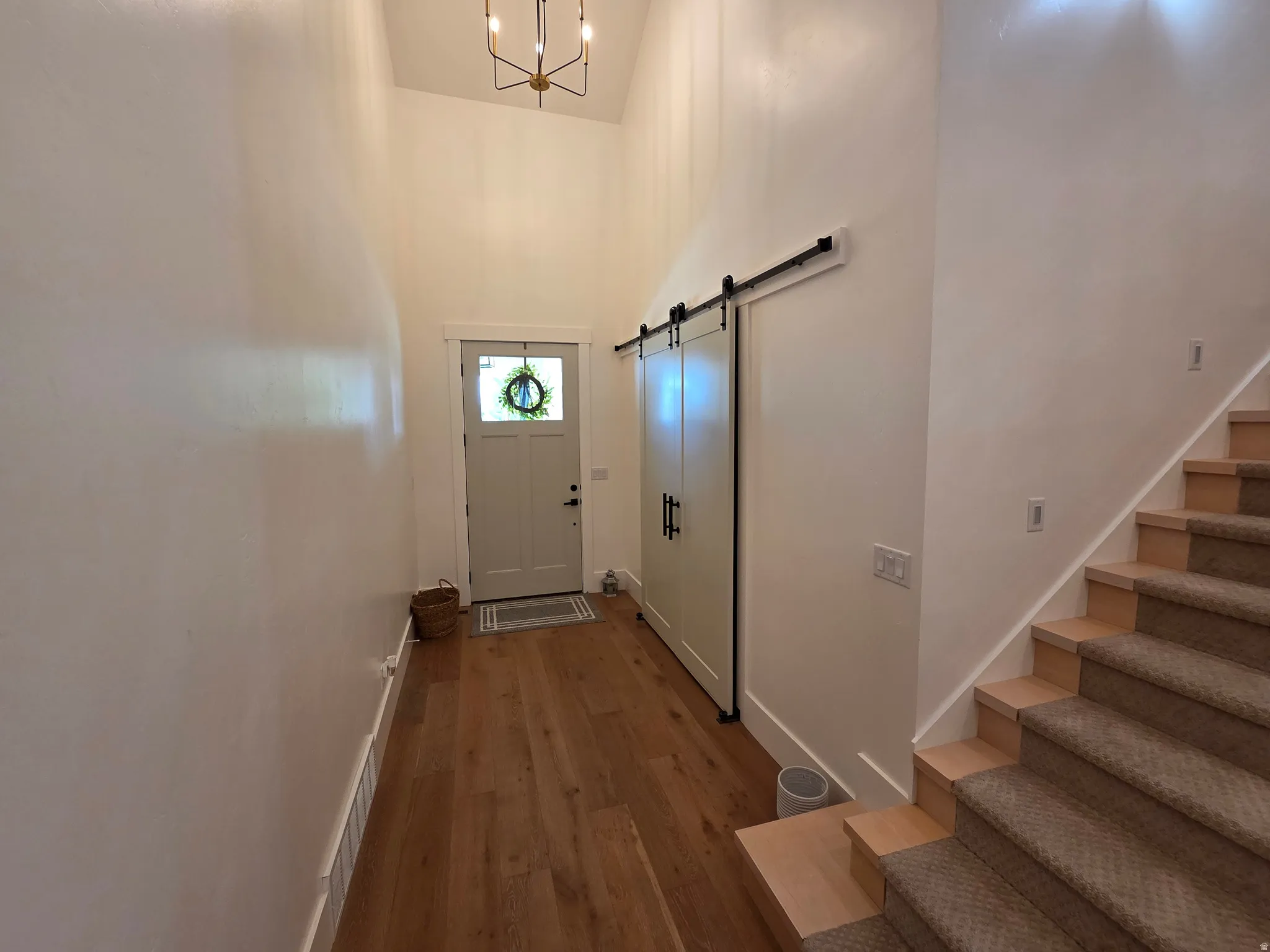 Welcoming foyer featuring wood-finish flooring, soaring ceiling height with pendant lighting, barn-style sliding door, and direct access to staircase