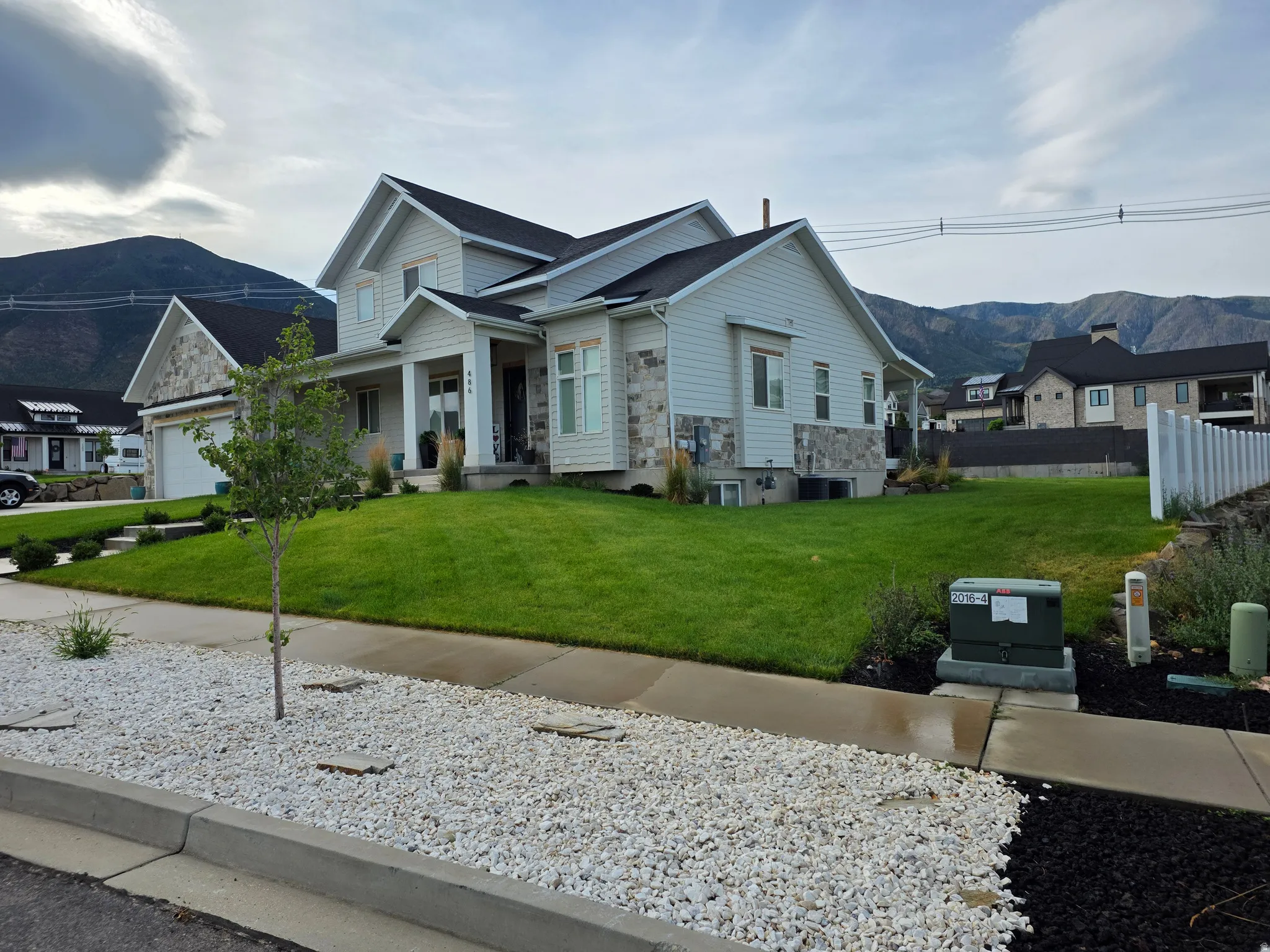 Modern farmhouse with light exterior siding, multi-gabled roofline with dark asphalt shingles, and large front-facing windows