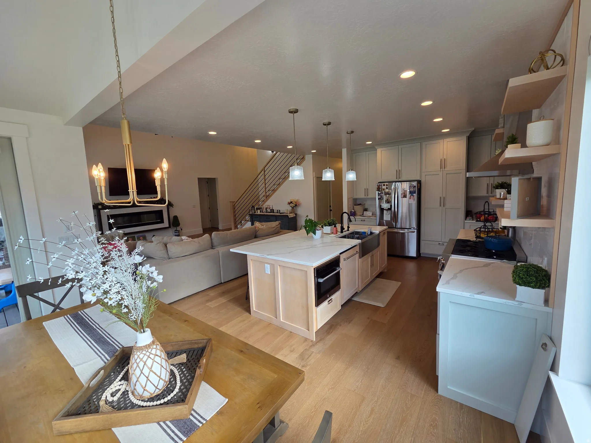 Open-concept living space featuring wood-finish flooring, a kitchen island with integrated microwave, recessed lighting, and a linear electric fireplace