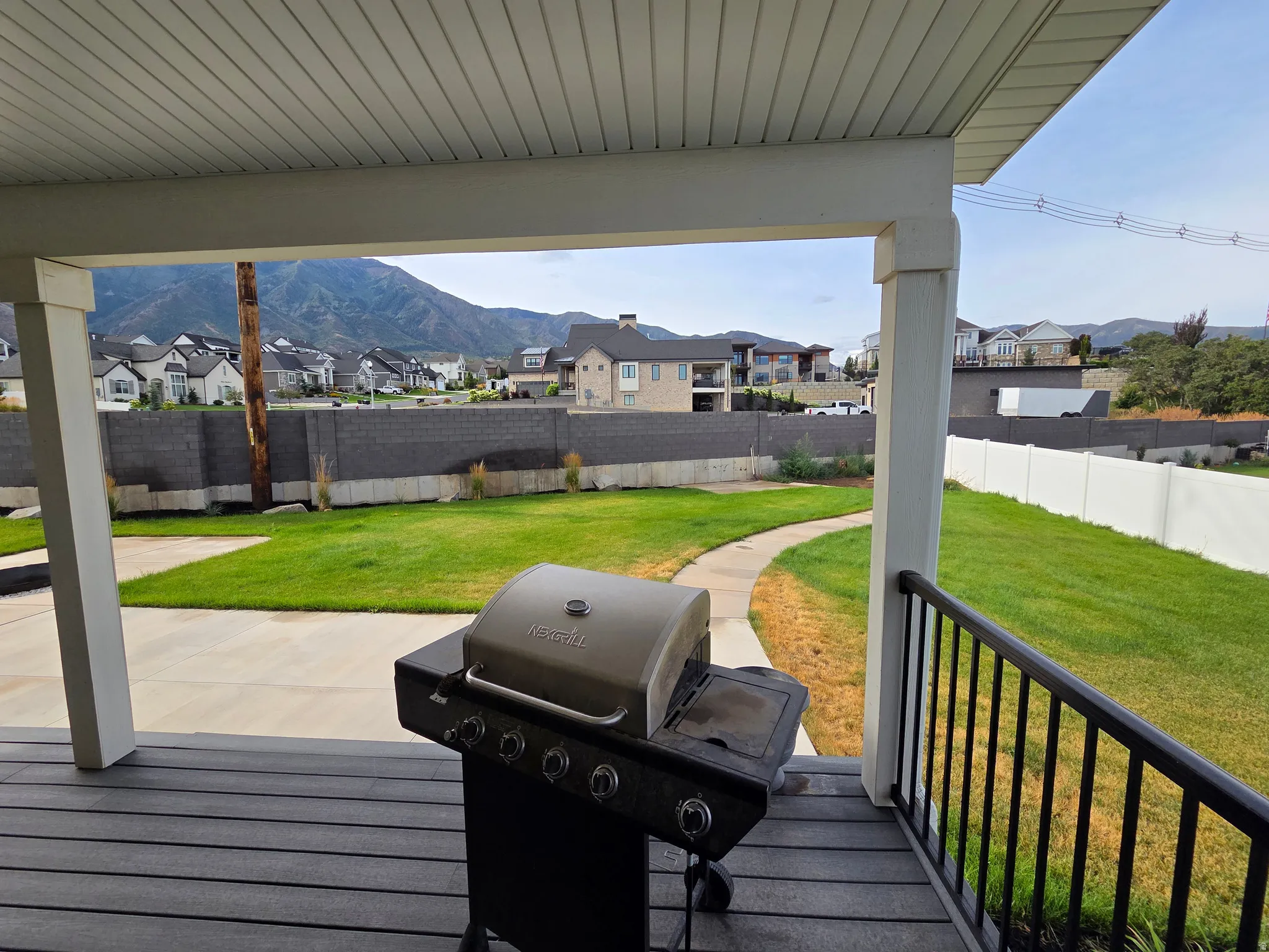Covered composite deck with built-in gas grill featuring multiple burners and control knobs, overlooking a spacious manicured lawn