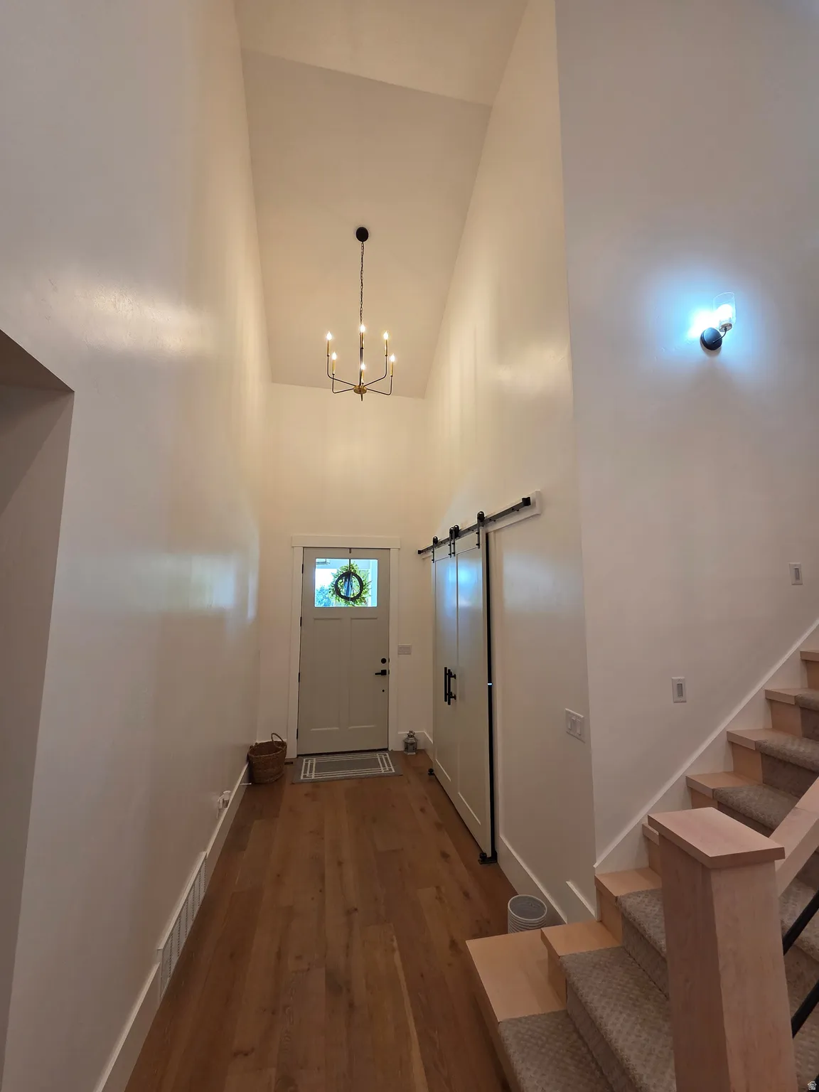 Welcoming foyer showcasing soaring vaulted ceilings, warm wood-finish flooring, and a modern pendant light fixture