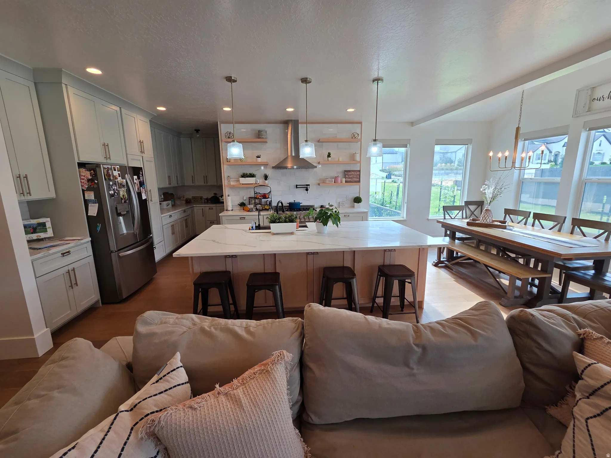 Open-concept living space featuring a chef's kitchen with white cabinetry, stainless steel appliances, large waterfall-edge island with seating for four, and abundant natural light from expansive windows