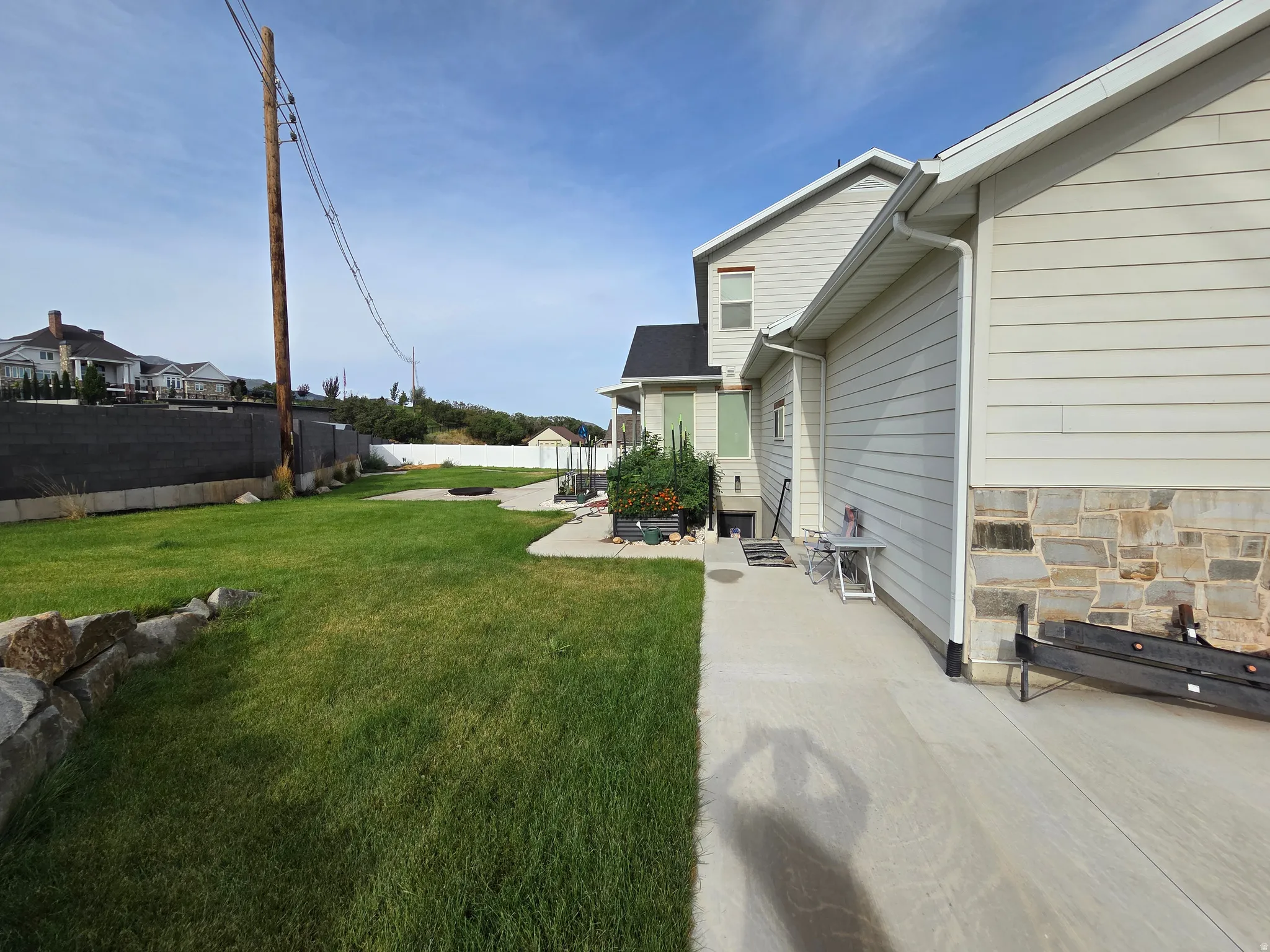 Expansive green lawn, concrete patio, stone foundation accents, and horizontal siding