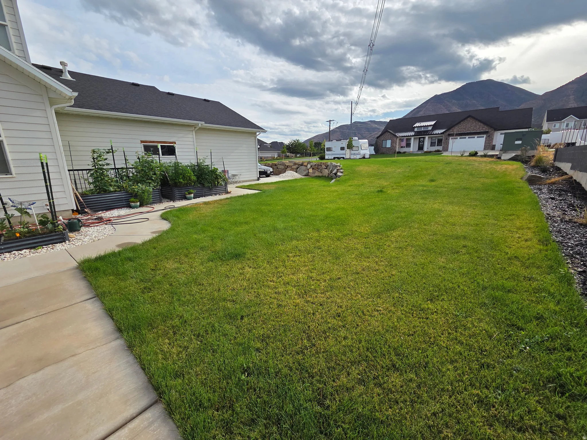 Expansive lawn with lush green turf, concrete patio with curved landscaping beds, and mature trees providing natural screening