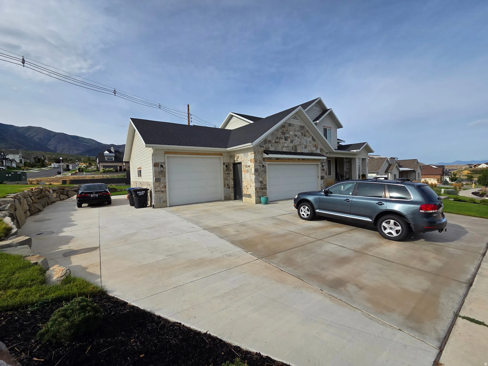 Stone and siding exterior with a multi-car concrete driveway, attached two-car garage, and a stacked stone retaining wall
