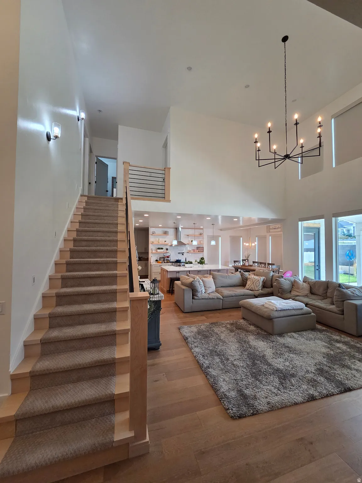 Soaring two-story great room with expansive windows and natural light, anchored by a modern chandelier fixture