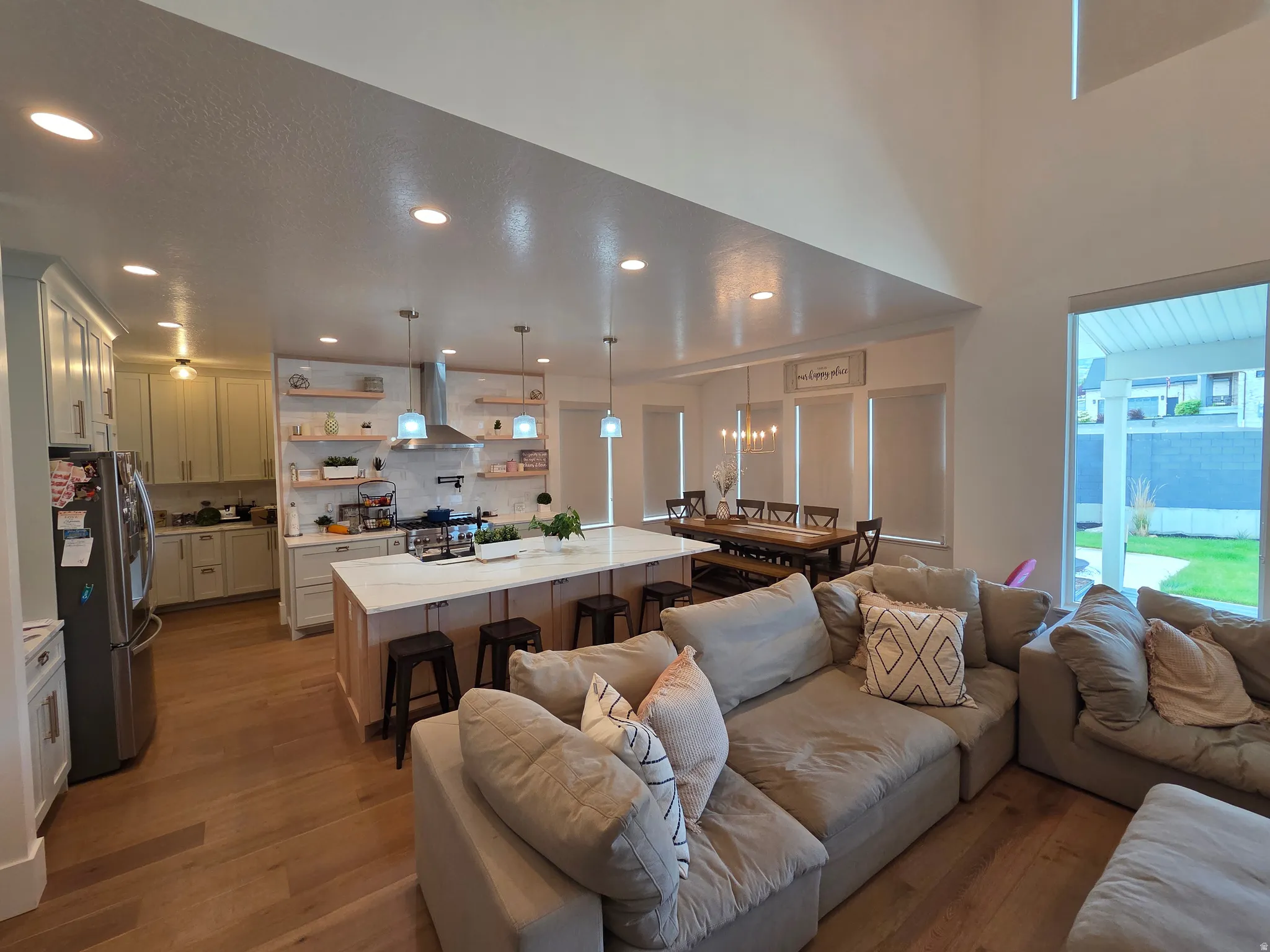 Open-concept living featuring a spacious kitchen with stainless steel appliances, white cabinetry, and a large island with seating, combined with a generous great room anchored by recessed and pendant lighting, wood-finish flooring throughout, and abundan