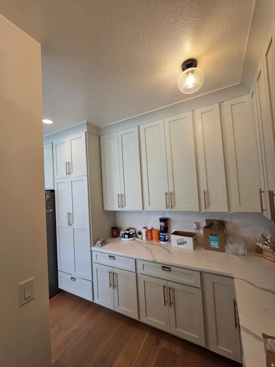 Bright and functional kitchen featuring white shaker-style cabinetry with brushed metal hardware, wood-finish flooring, and ample countertop workspace