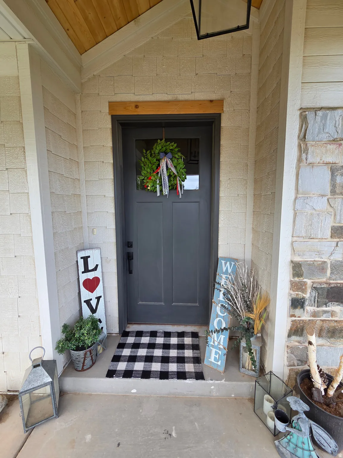 Welcoming entry featuring a dark-finish six-panel door with transom window, black-and-white checkered tile flooring, white painted brick exterior, and decorative wreath accent