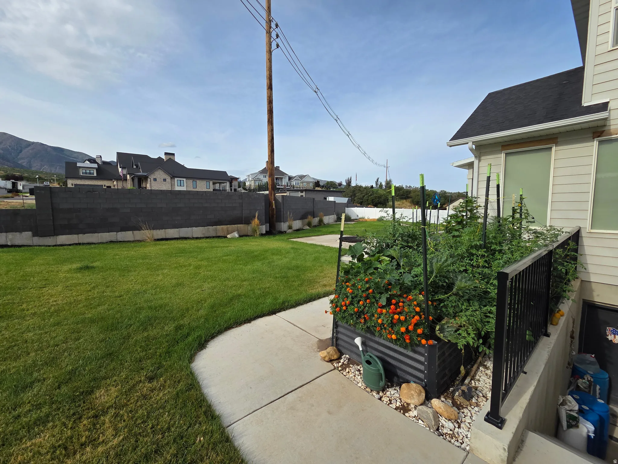 Manicured lawn, concrete pathway, raised garden bed, and a low-profile privacy wall