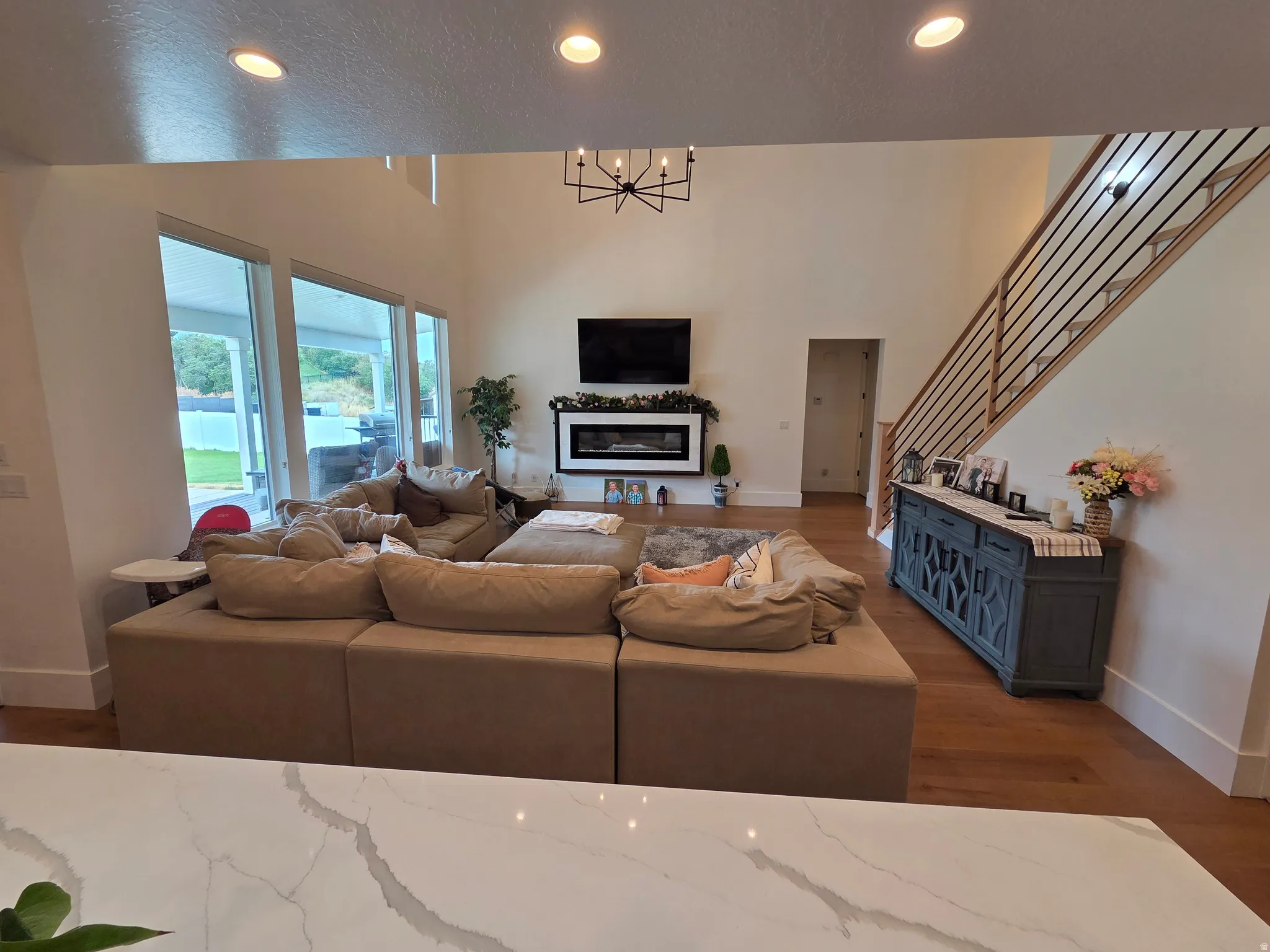 Open-concept living area featuring a spacious sectional layout, wood-finish flooring throughout, and abundant natural light from large glass doors