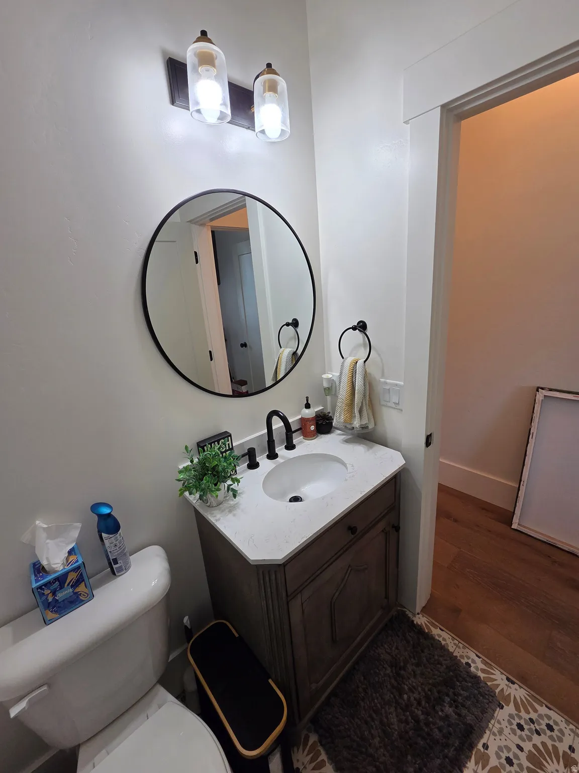 Modern bathroom vanity featuring a white porcelain sink, wood-finish cabinetry with ample storage, and a sleek round mirror with metal framing