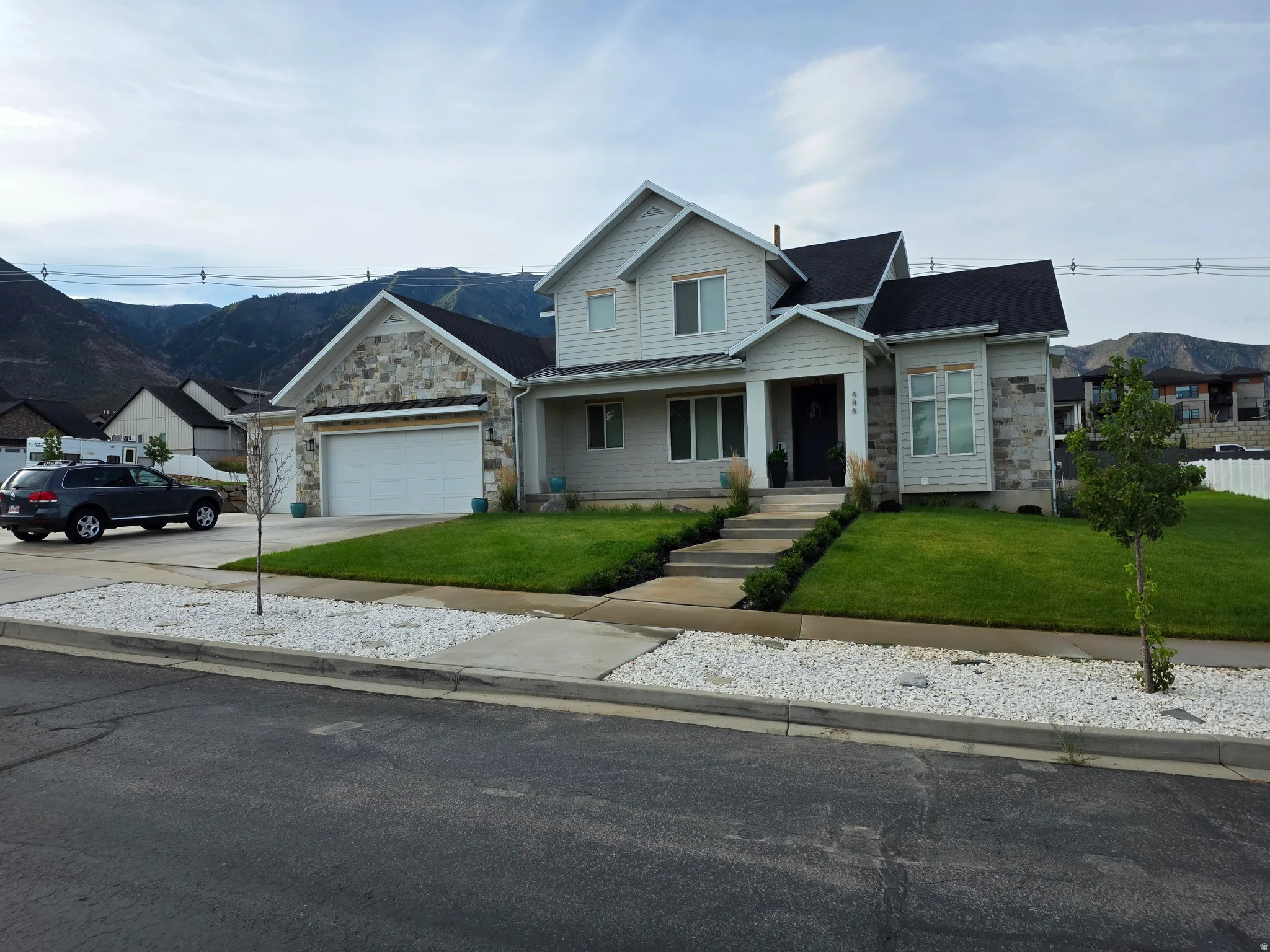Two-story residence featuring a stone and siding exterior with a two-car garage, manicured lawn, and established landscaping
