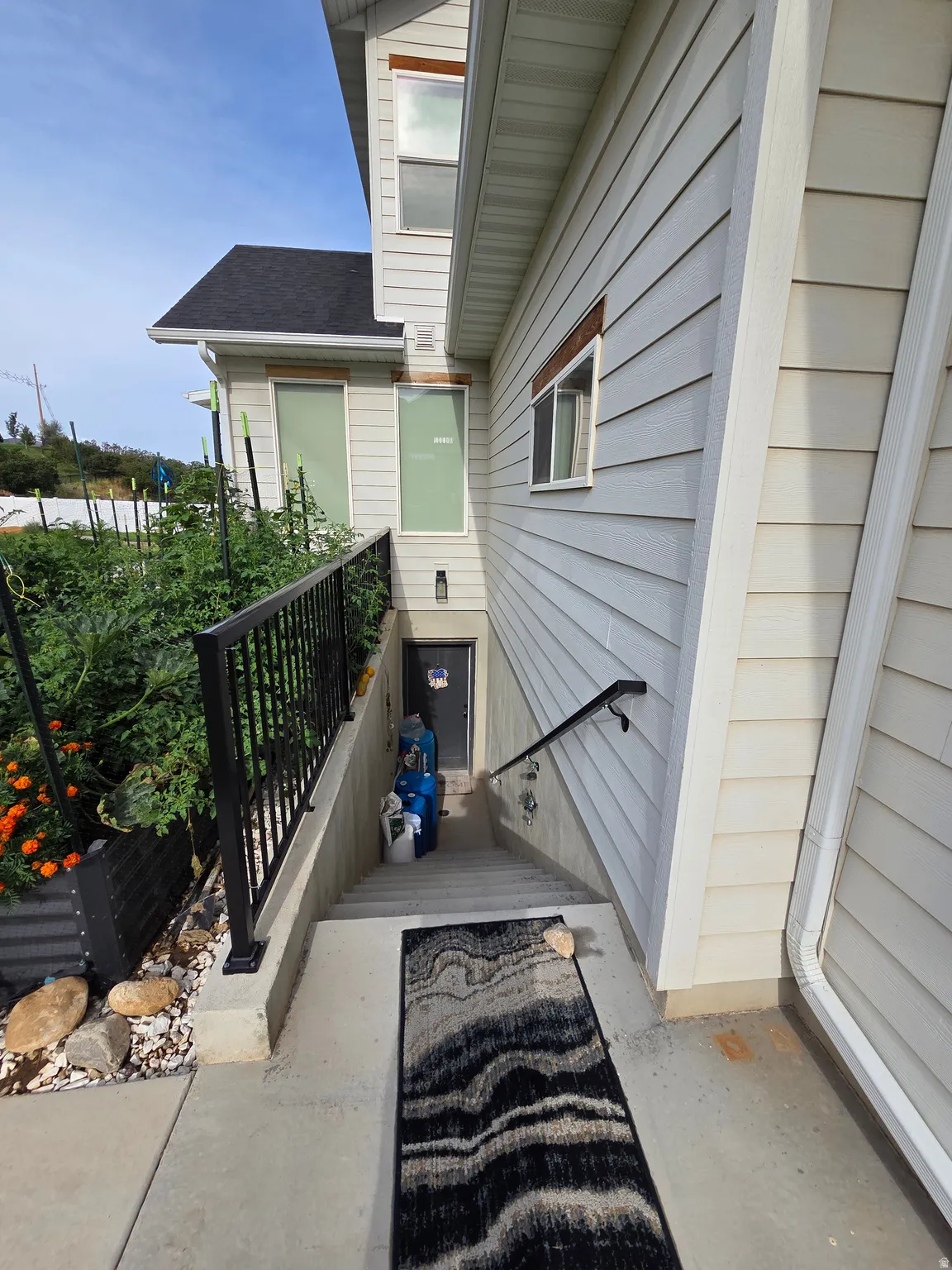 Charming side entry featuring a concrete walkway, black metal railing, and mature landscaping