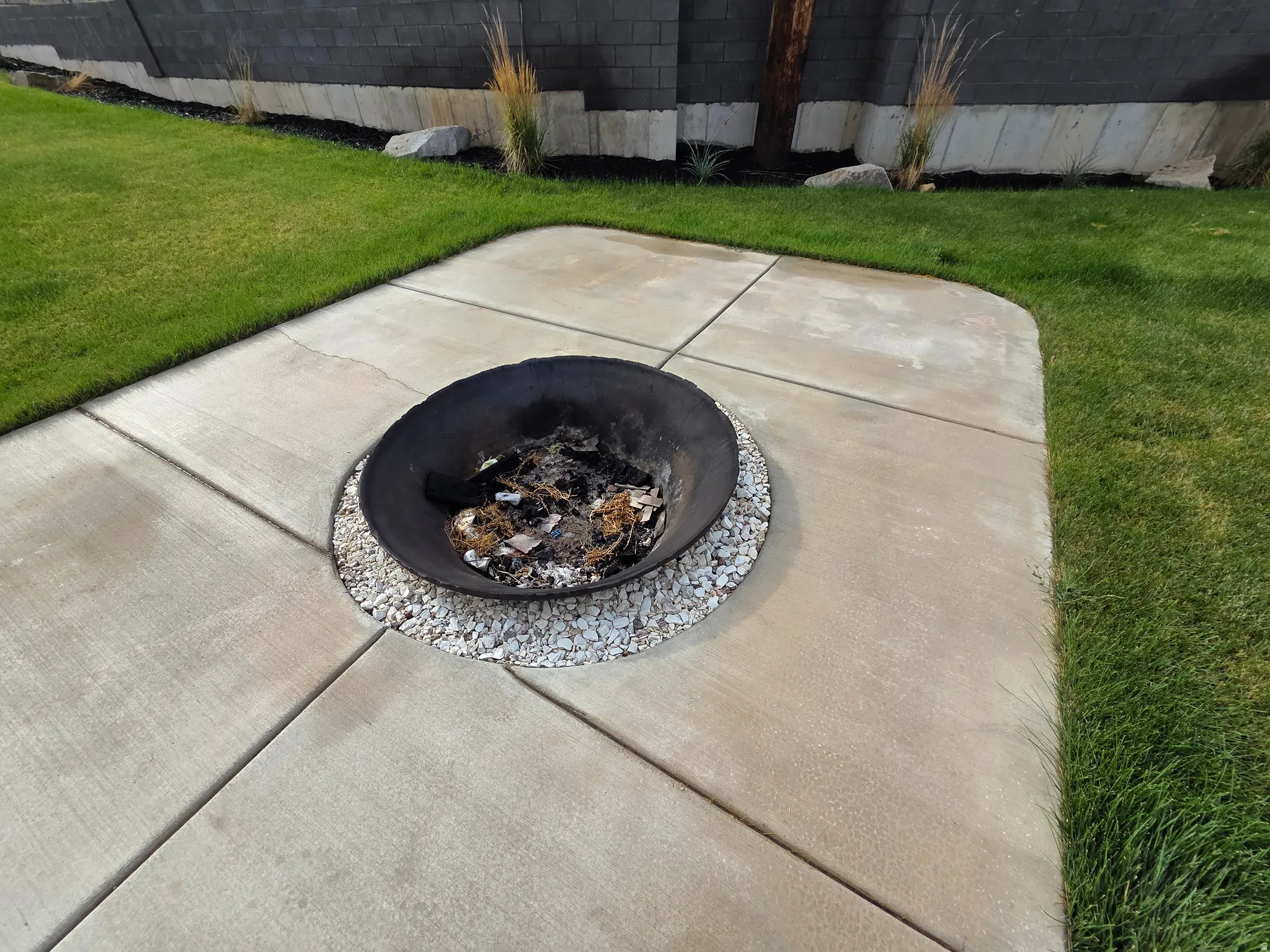 Expansive concrete patio with geometric scoring detail, anchoring a manicured lawn bordered by mature landscaping and ornamental grasses