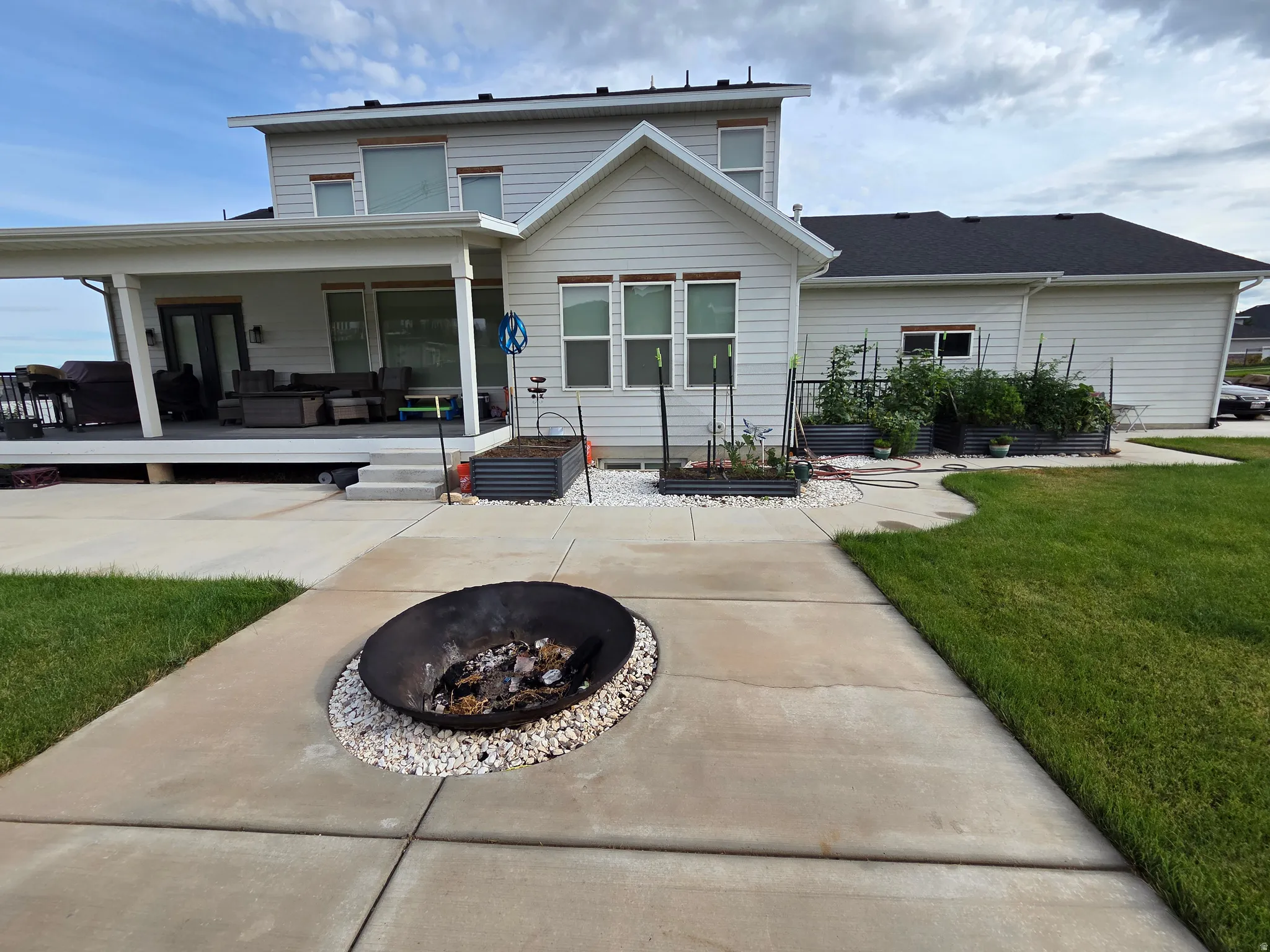 Charming farmhouse-style residence with expansive concrete patio, integrated fire pit surround with decorative stone edging, and manicured lawn