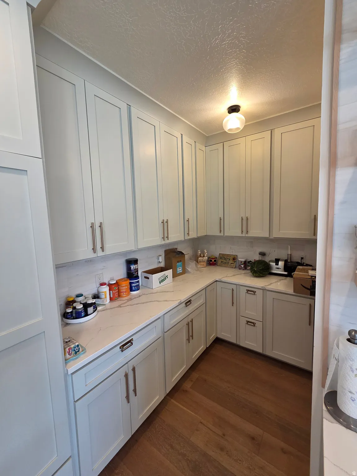Efficient galley-style kitchen featuring white cabinetry with brushed nickel hardware, light countertops, wood-finish flooring, and recessed ceiling lighting