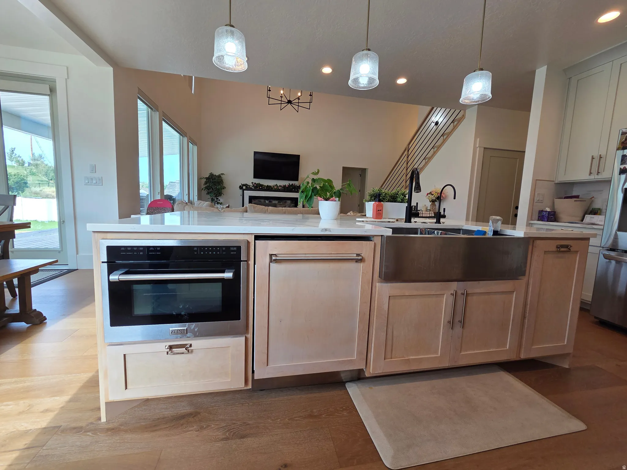 Expansive kitchen island featuring a farmhouse sink, stainless steel appliances, and pendant lighting