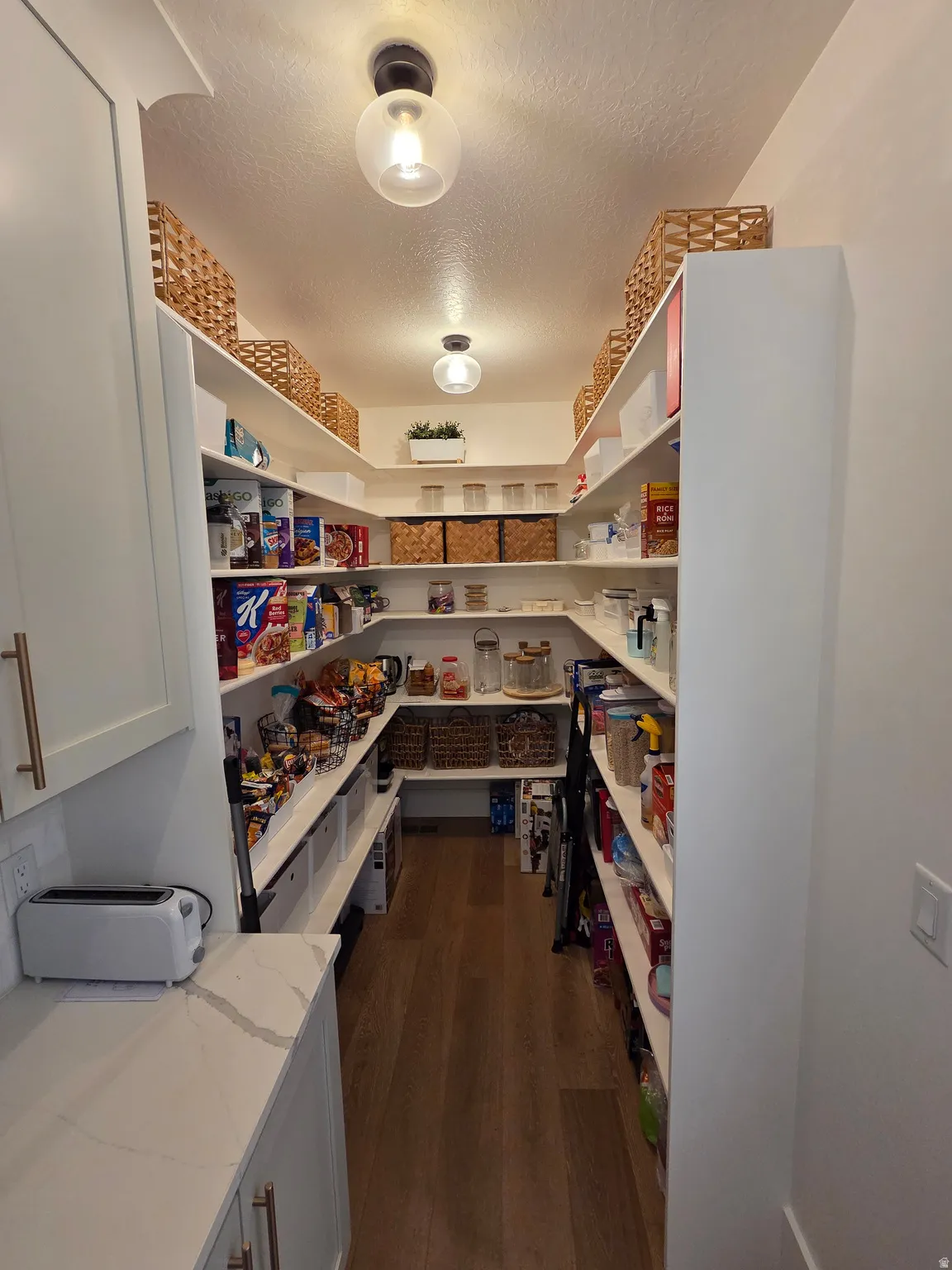 Spacious pantry with extensive shelving throughout, wood-finish flooring, and recessed ceiling lighting
