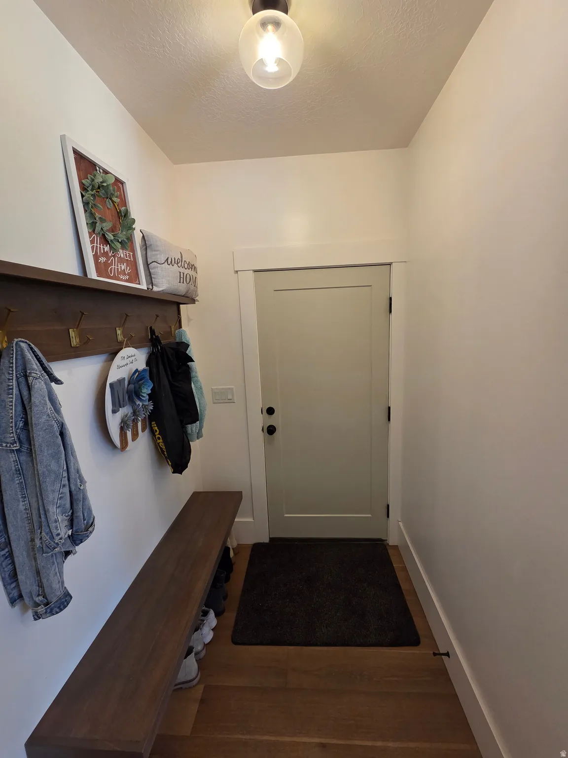 Welcoming entryway featuring warm wood-finish flooring, a built-in bench with storage, wall-mounted coat hooks, and a solid-core interior door