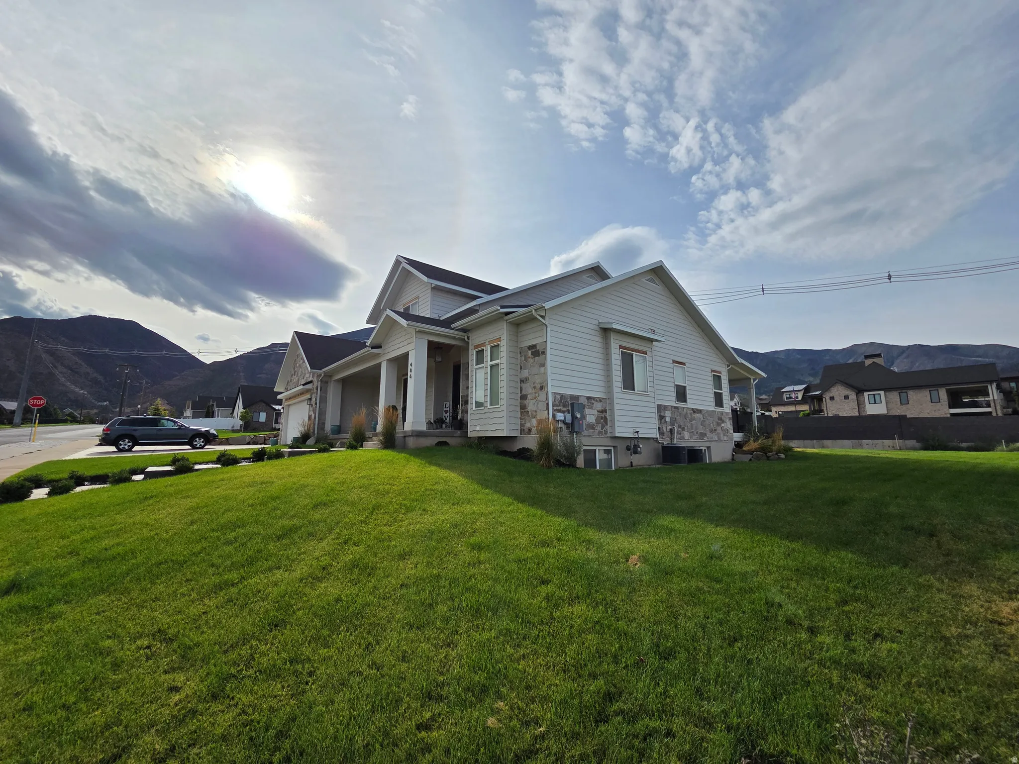 Contemporary exterior with light siding, stone accents, a covered entry, an attached garage, and a manicured lawn