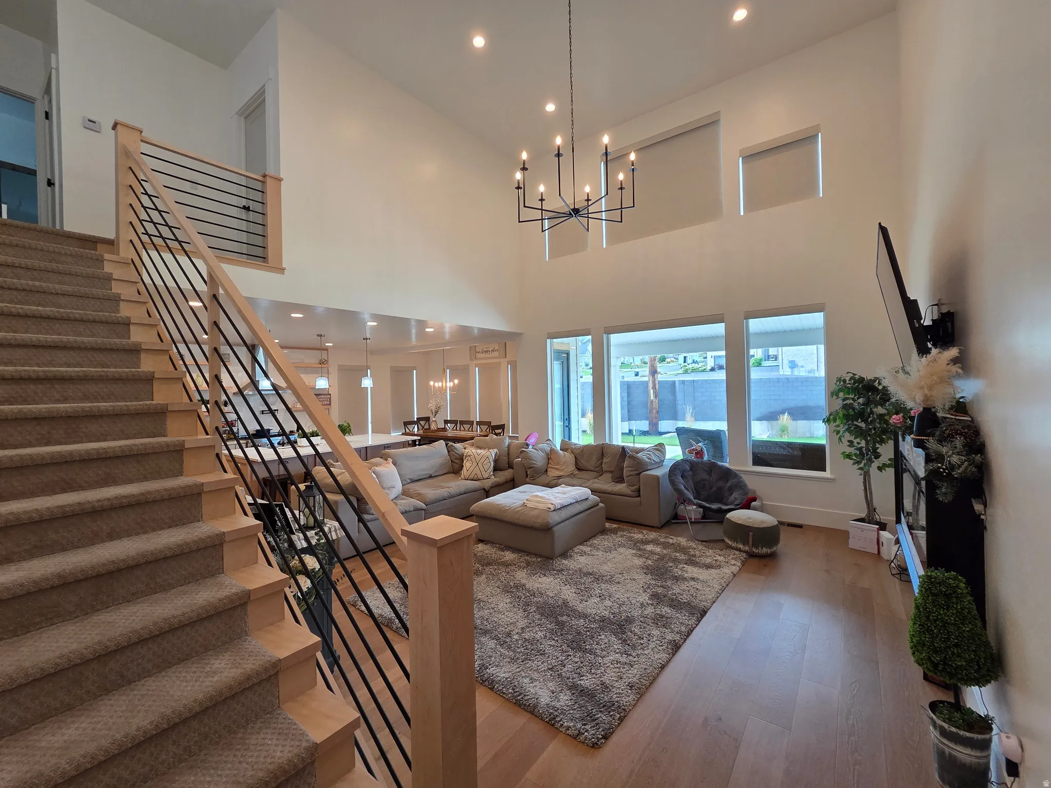 Vaulted ceilings, a contemporary chandelier, recessed lighting, wood-finish flooring, and a modern horizontal slat railing system