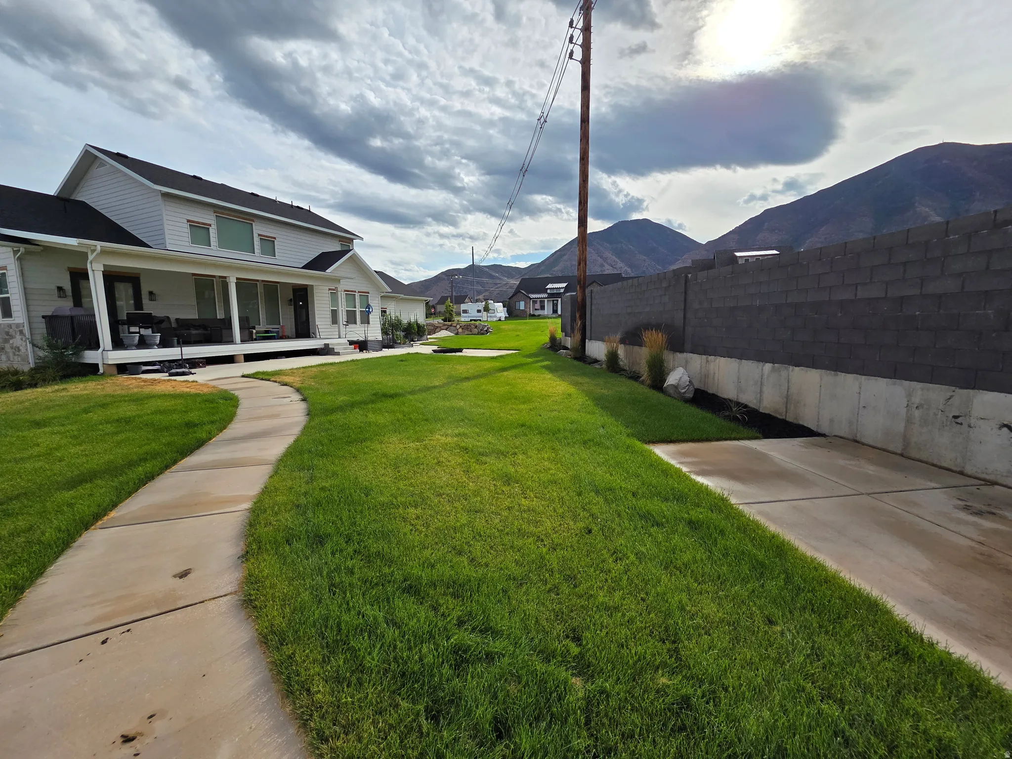 Manicured lawn with concrete walkway leading to modern farmhouse-style residence featuring a covered front porch, white exterior trim, and mountain backdrop