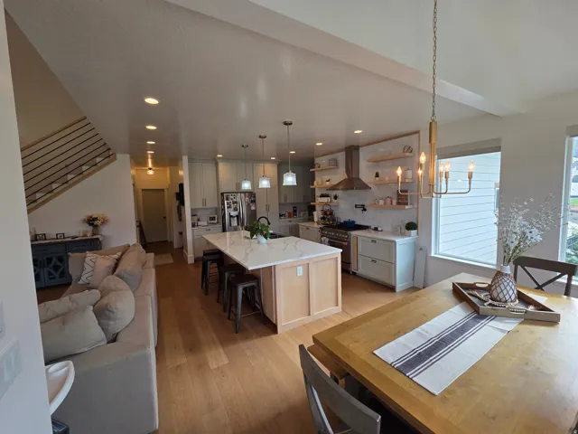Open-concept kitchen and dining area featuring a large center island with seating, white cabinetry, stainless steel appliances, and wood-finish flooring throughout