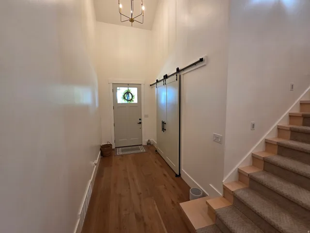 Welcoming foyer featuring wood-finish flooring, soaring ceiling height with pendant lighting, barn-style sliding door, and direct access to staircase