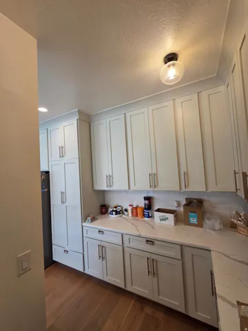 Bright and functional kitchen featuring white shaker-style cabinetry with brushed metal hardware, wood-finish flooring, and ample countertop workspace