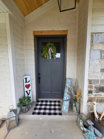 Welcoming entry featuring a dark-finish six-panel door with transom window, black-and-white checkered tile flooring, white painted brick exterior, and decorative wreath accent