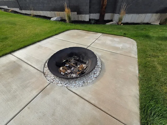 Expansive concrete patio with geometric scoring detail, anchoring a manicured lawn bordered by mature landscaping and ornamental grasses