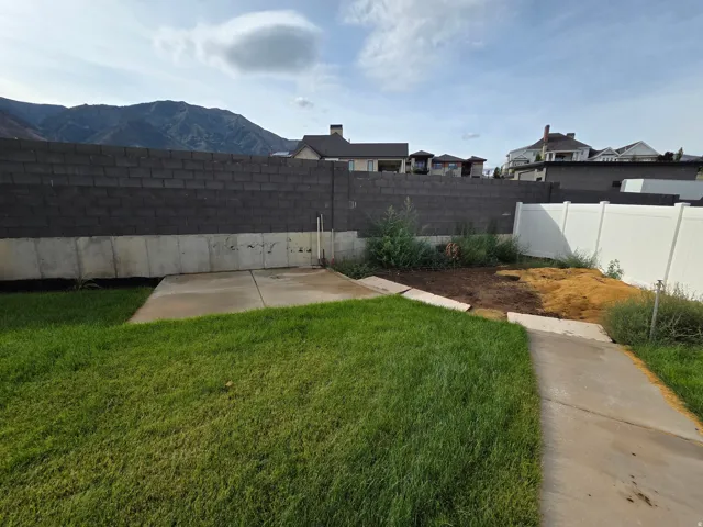 Spacious backyard with mature lawn, concrete pathways, and dedicated garden bed area