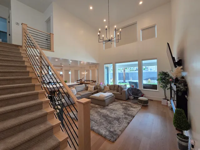 Vaulted ceilings, a contemporary chandelier, recessed lighting, wood-finish flooring, and a modern horizontal slat railing system