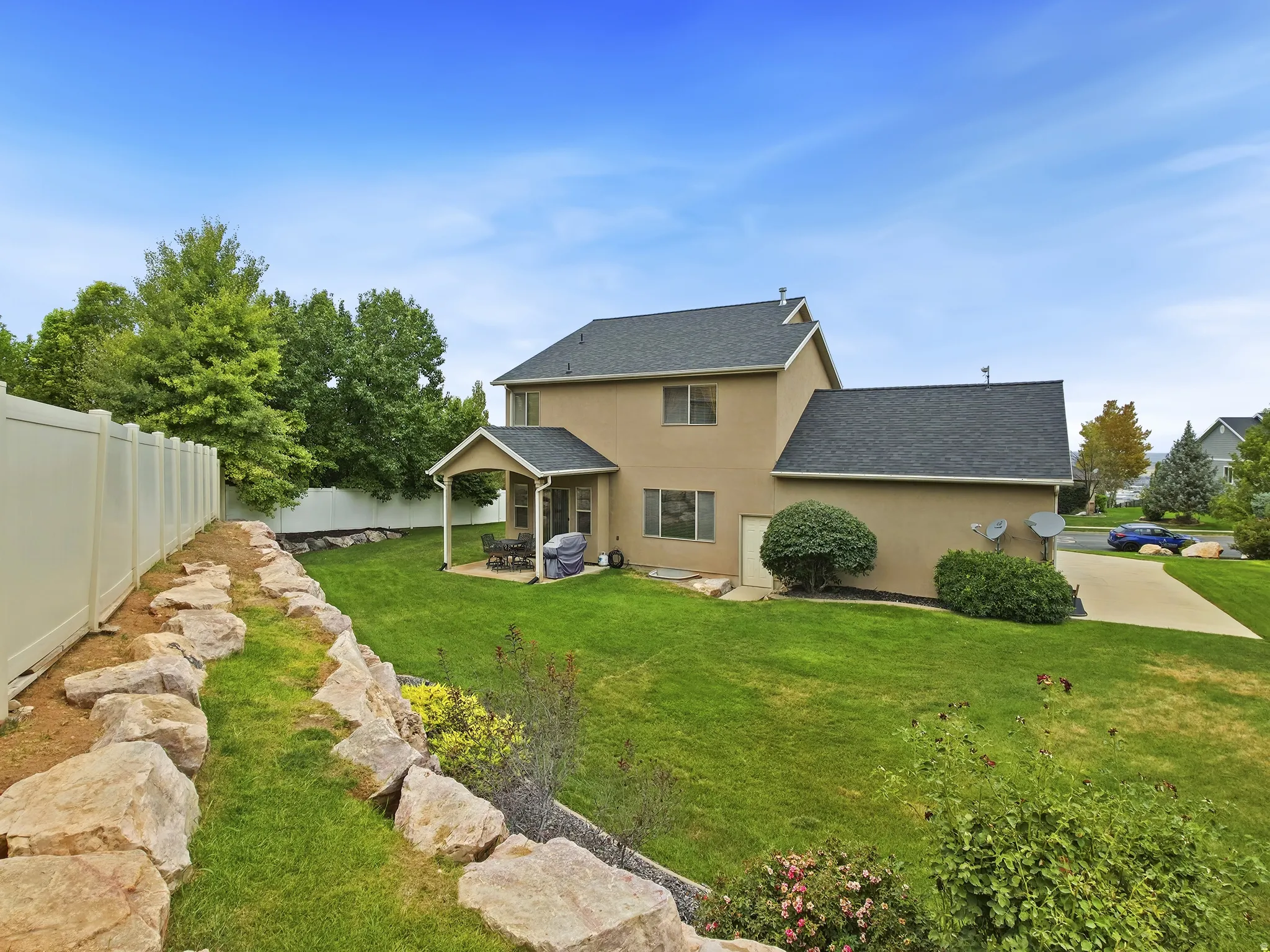 Expansive backyard featuring a manicured lawn, a covered patio, and a rock retaining wall