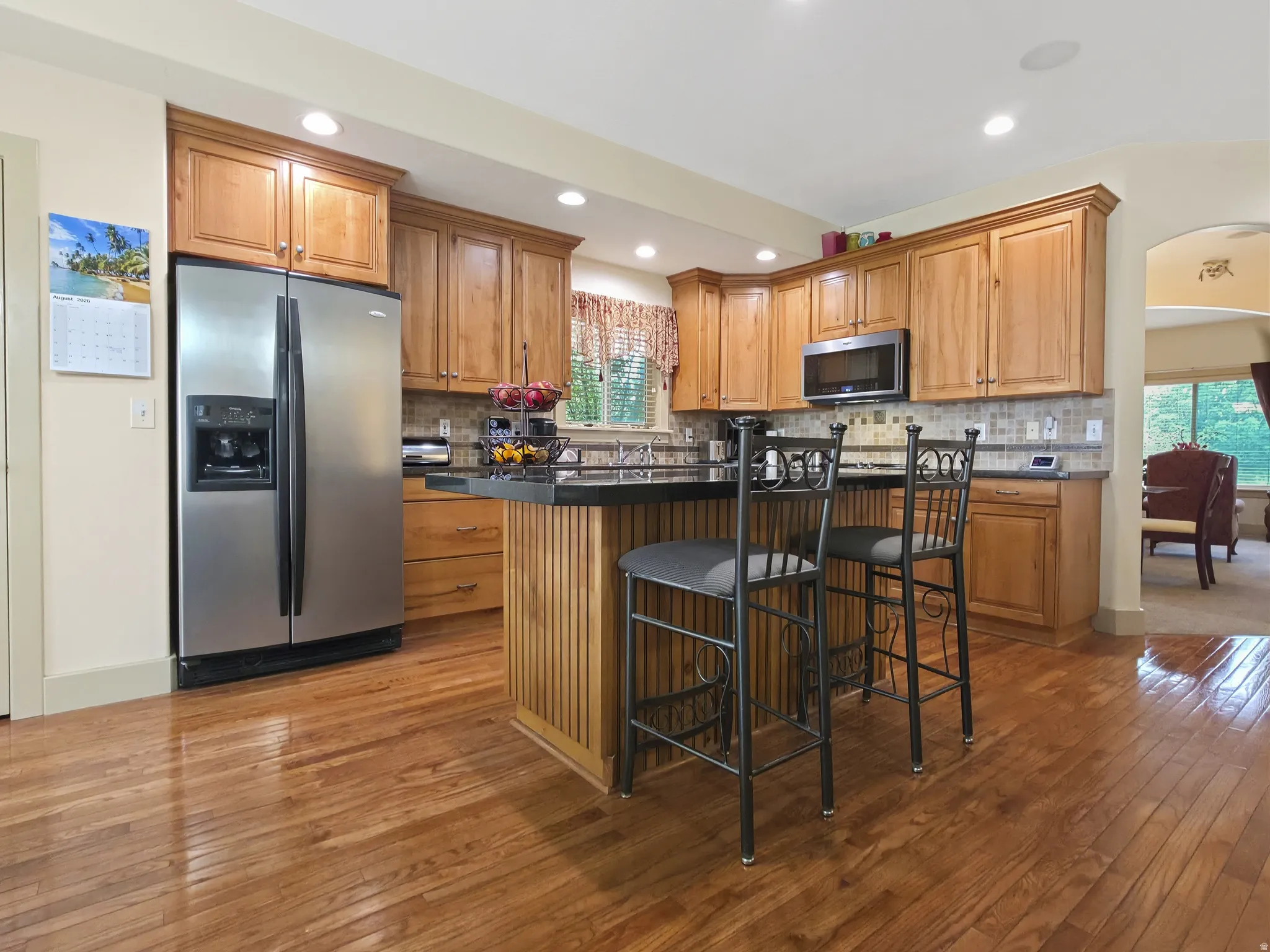 Wood-finish flooring, recessed lighting, wood cabinetry, stainless steel refrigerator, and a kitchen island with seating