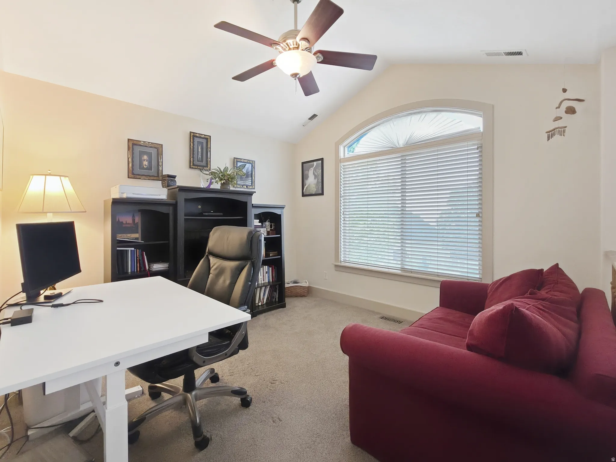 Vaulted ceiling with a ceiling fan, arched window with horizontal blinds, built-in black shelving units, and neutral carpeting