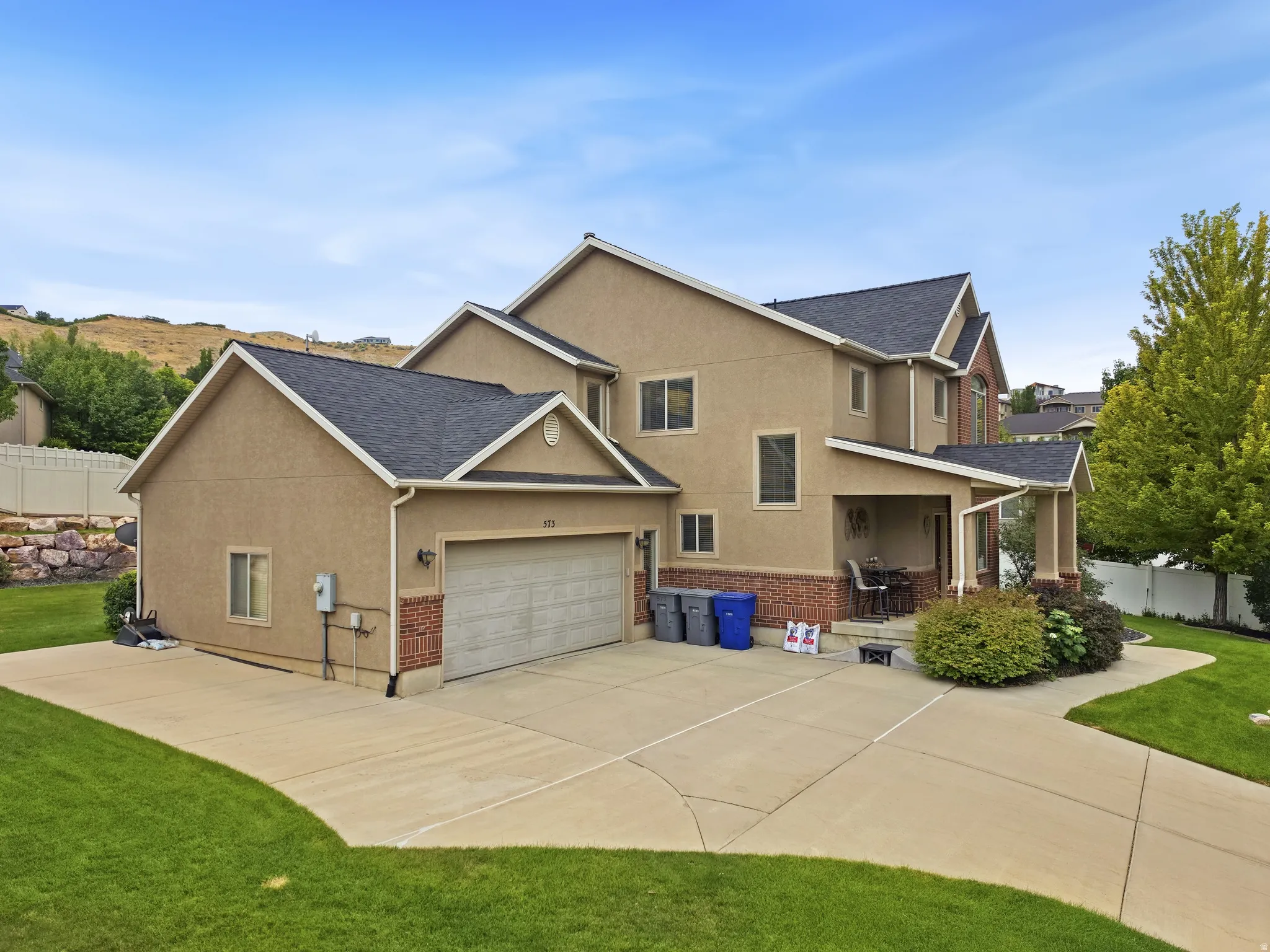 Stucco exterior with brick detailing, multi-pitched shingle roof, attached garage, covered porch, and concrete driveway