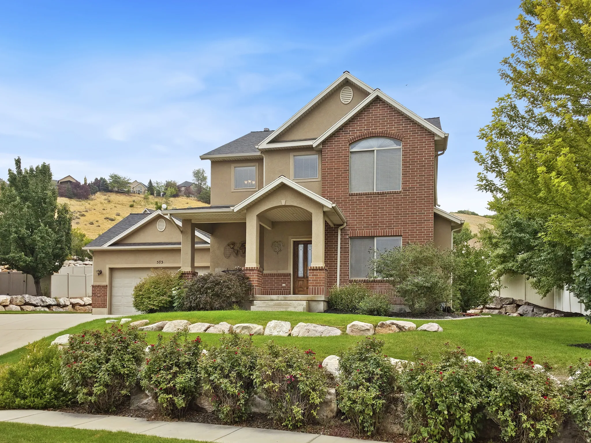 Brick and stucco exterior, arched front entry, attached garage, well-maintained landscaping, and a manicured lawn