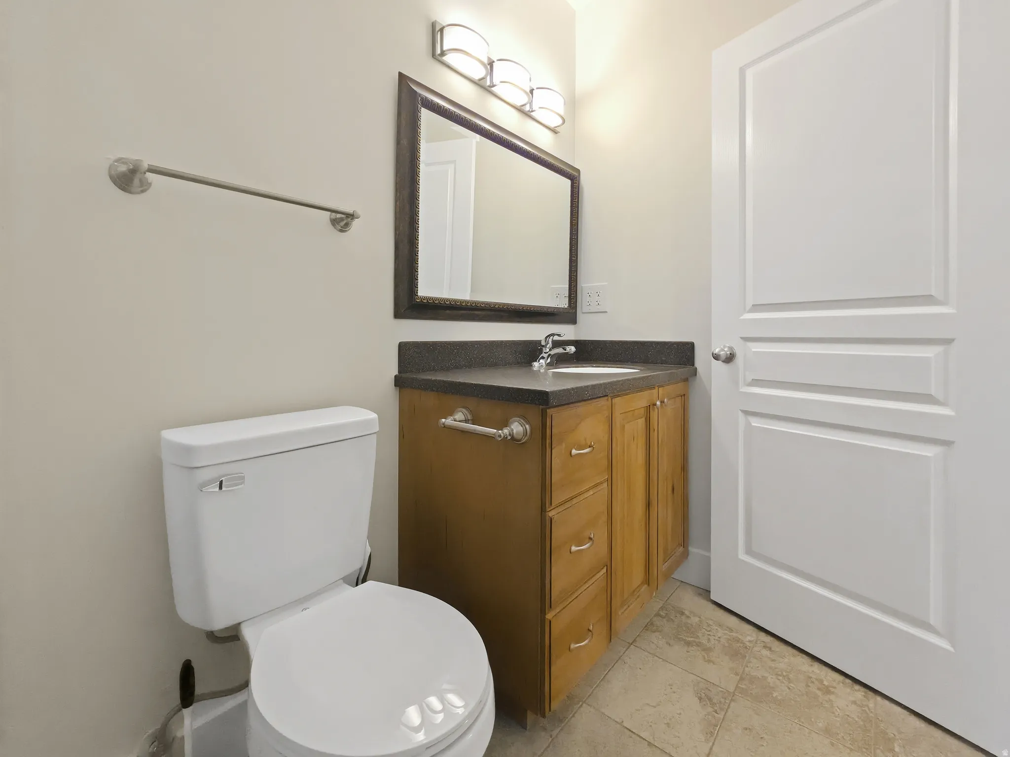 Vanity with wood-finish cabinetry, dark countertop, and integrated sink
