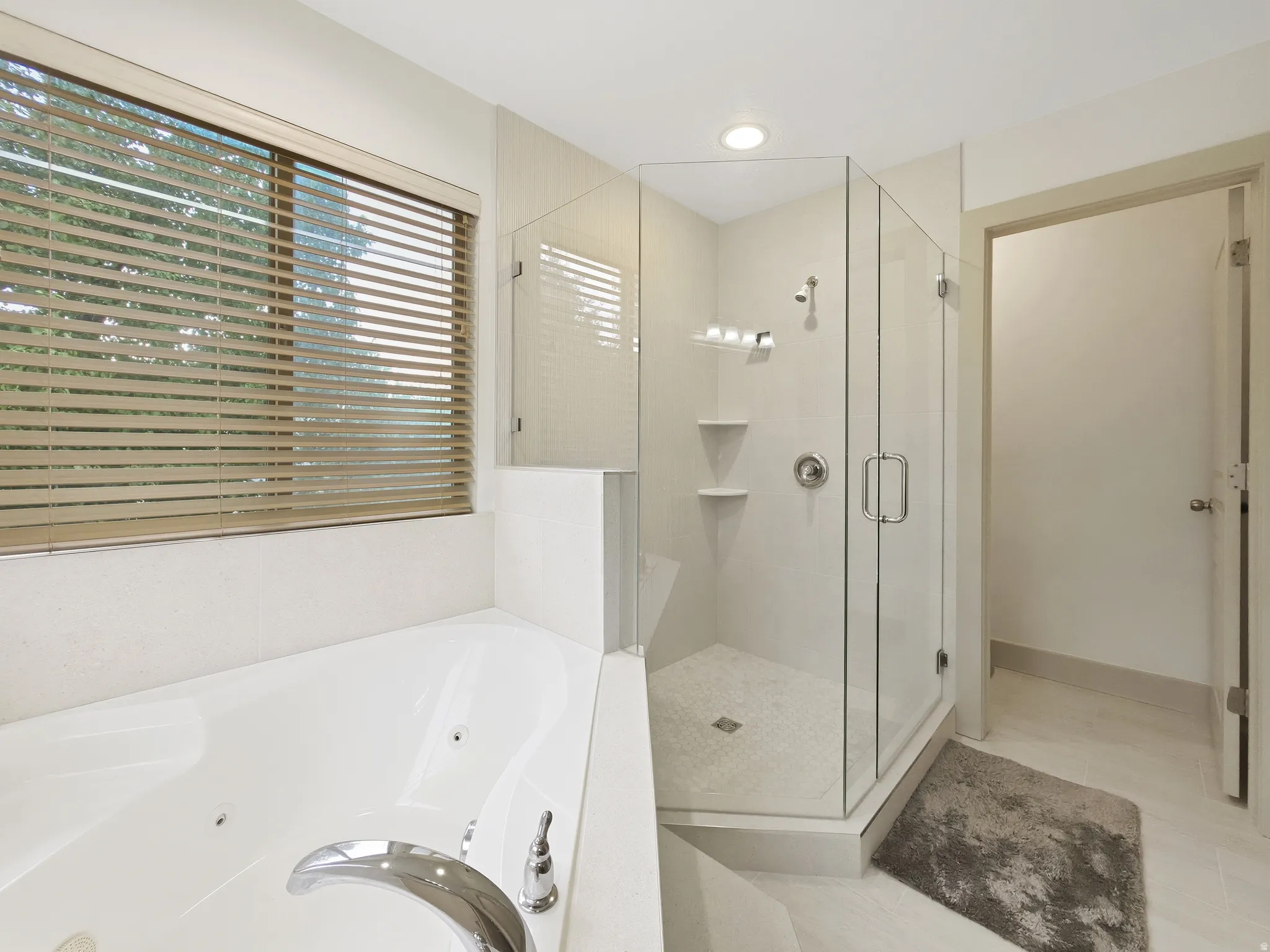 Soaking tub with chrome fixtures, glass-enclosed shower, built-in shower shelving, and neutral tile flooring
