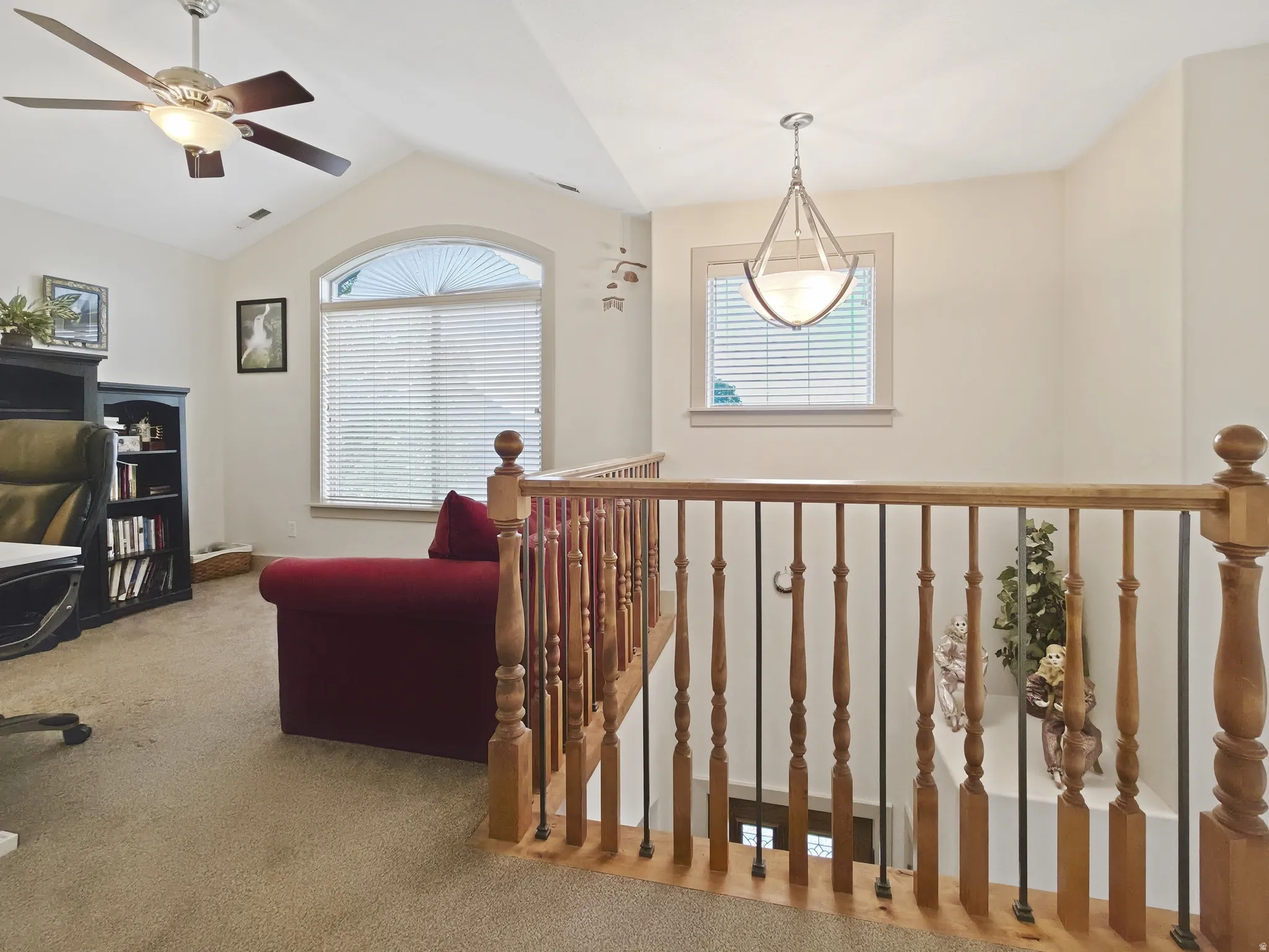 Vaulted ceiling with ceiling fan, arched window, wood and iron spindle railing, recessed window, and pendant light fixture