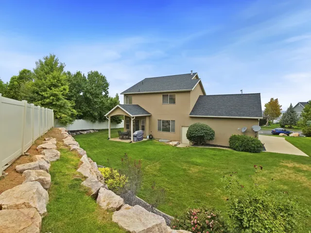 Expansive backyard featuring a manicured lawn, a covered patio, and a rock retaining wall