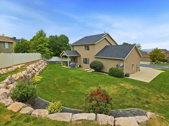 Expansive green lawn, extensive rock landscaping, mature shrubbery, covered patio, and a privacy fence
