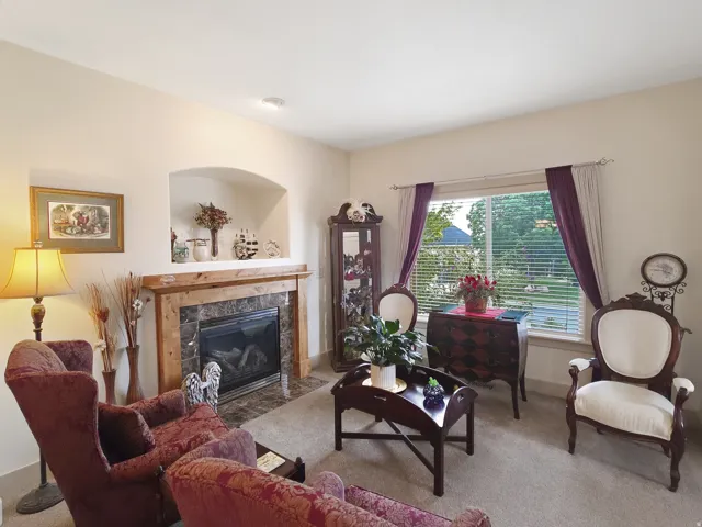 Carpeted living area featuring a fireplace with a wood-finish mantel and stone surround, an arched wall niche, and a window with blinds