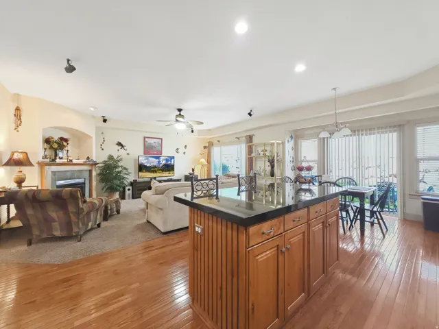 Hardwood flooring, kitchen island with dark countertop, built-in cabinetry, recessed lighting, and a fireplace with a stone surround
