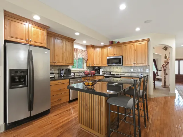 Hardwood flooring, wood cabinetry with crown molding, stainless steel appliances, black countertops, and a tiled backsplash