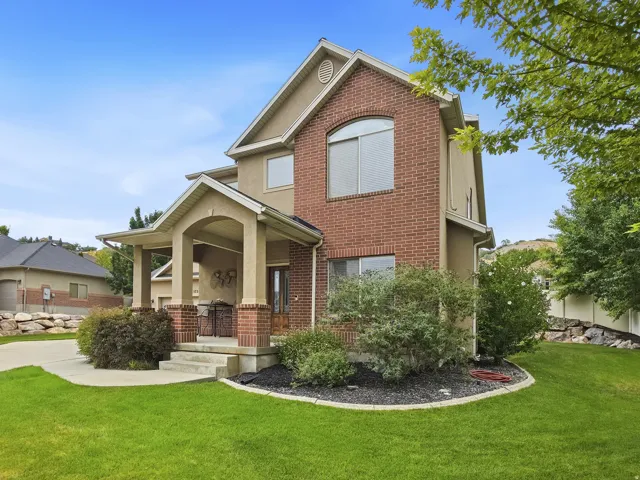 Stucco and brick exterior with arched window, covered porch entry, concrete driveway, and manicured lawn