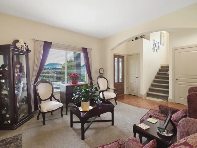 Carpeted living area with a large window, a wood-finish entry door with frosted glass, and an arched doorway leading to a staircase with carpeted treads